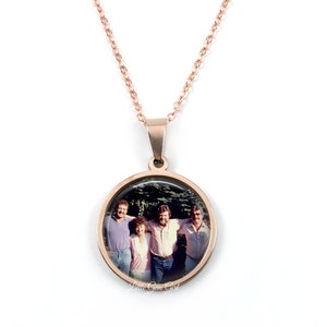 May include: A rose gold necklace with a round pendant featuring a photo of four people. The pendant has a clear glass cover.