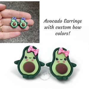 May include: A pair of avocado earrings with pink and white polka dot bows. The earrings are green with brown avocado pits and have a cute cartoon face.