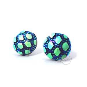 May include: A pair of round stud earrings with a blue and green iridescent pattern. The pattern resembles a reptile skin.