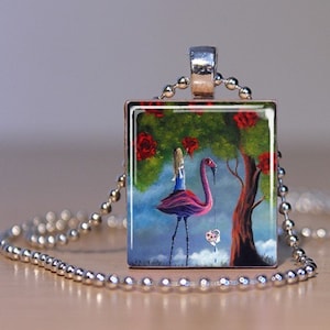 Könnte beinhalten: Quadratische Anhänger-Halskette mit einer fantastischen Illustration eines Flamingos, der eine Person trägt, unter einem Baum mit roten Rosen. Der Anhänger hängt an einer silbernen Kugelkette.