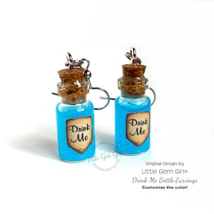 May include: A pair of blue glass bottle earrings with cork stoppers and silver hooks. The bottles have a label that says "Drink Me".