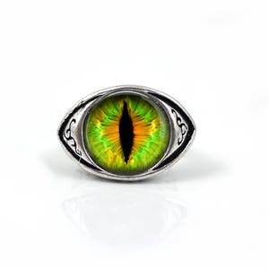 May include: A silver ring with a green and yellow eye design. The eye has a black pupil and a silver ring around it.
