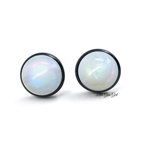 Pu&ograve; includere: Un paio di orecchini a bottone bianchi iridescenti con montature in metallo nero.