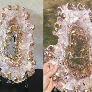 May include: A white and gold resin geode tray with pink glitter and pink crystals. The tray is on a black stand and has the text "Little Gem Girl" on the bottom.