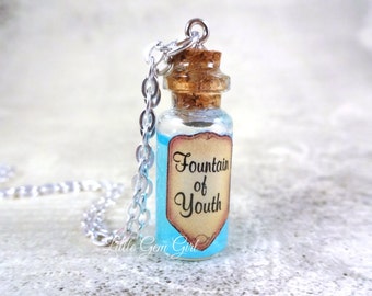 May include: A silver chain necklace with a small glass bottle pendant. The bottle is filled with a light blue liquid and has a cork stopper. A label on the bottle reads "Fountain of Youth".