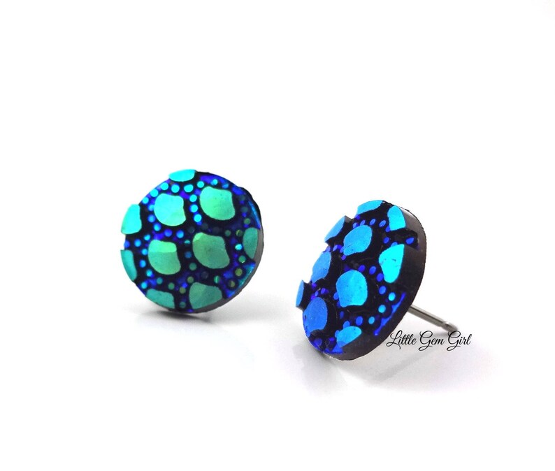 May include: A pair of blue and green iridescent stud earrings with a textured, scaly design. The earrings are made of polymer clay and have a silver post.