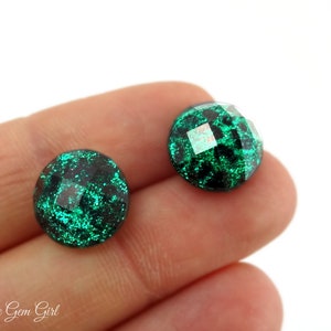 May include: A pair of green glitter earrings with a faceted design. The earrings are round and have a dark green base with a light green glitter overlay.