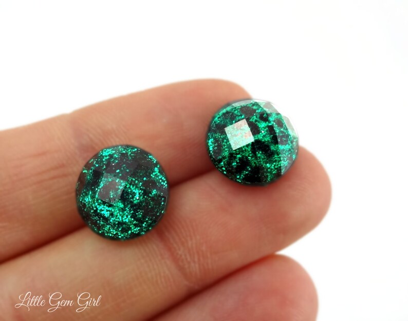 May include: A pair of green glitter earrings with a faceted design. The earrings are round and have a dark green base with a light green glitter overlay.