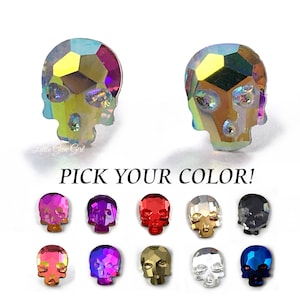 May include: A pair of iridescent skull stud earrings. The earrings are available in a variety of colors, including red, pink, purple, blue, green, gold, silver, and black. "Pick Your Color!" is written below the earrings.