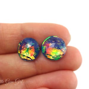 May include: A pair of iridescent opal earrings with a blue, green and orange colour scheme. The earrings are round and have a faceted design.