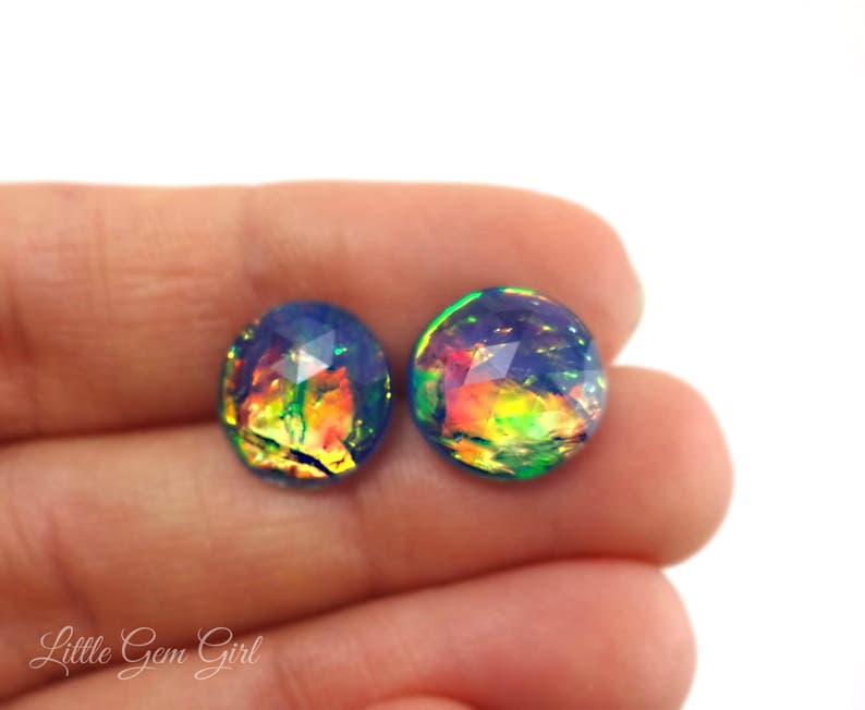 May include: A pair of iridescent opal earrings with a blue, green and orange colour scheme. The earrings are round and have a faceted design.