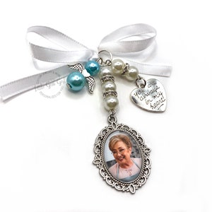 May include: A white satin ribbon with a silver charm featuring a photo of a woman. The charm is attached to a string of white pearls and a silver angel charm. The charm also has a silver heart with the inscription "You are always in my heart!"
