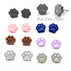 May include: A selection of paw print stud earrings in various colors, including gray, pink, blue, brown, purple, and silver. The text "Pick Your Color!" is displayed in the image. These earrings are a cute accessory for pet lovers.