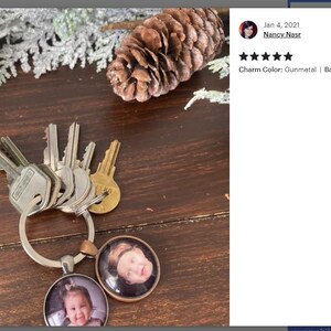 May include: A silver key chain with a gunmetal charm and two round photo inserts. The photo inserts feature pictures of children. The charm has the text "Charm Color: Gunmetal | Backside Design: D - Grey".