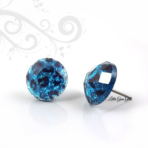 May include: A pair of blue and black glitter stud earrings with a leopard print design. The earrings are made of metal and have a post back.