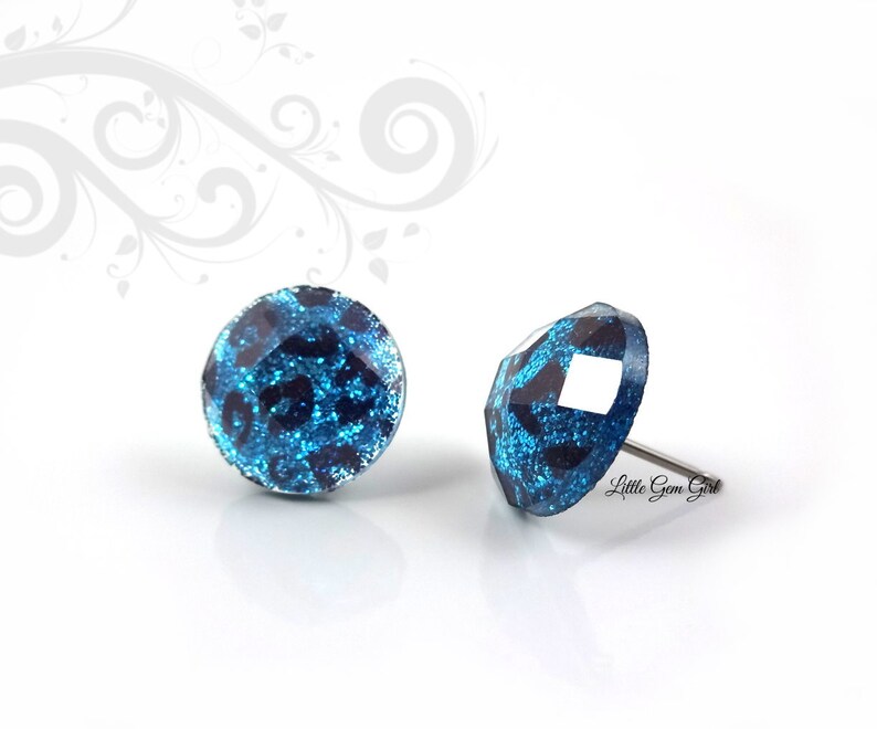 May include: A pair of blue and black glitter stud earrings with a leopard print design. The earrings are made of metal and have a post back.