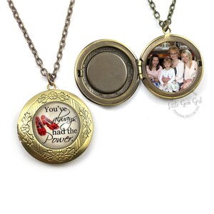 May include: A gold-toned locket necklace with a chain. The locket is open, revealing a photograph. The closed locket features the text "You've always had the Power" with an image of red shoes.