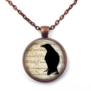 May include: A copper chain necklace with a round glass pendant featuring a black silhouette of a raven on a vintage-style paper background with text that reads "weak and wear", "volume of for", "While I nod", "As of someone", "is some visit", "Kerat", "P", "yu", "rap".
