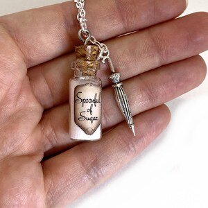 May include: A silver chain necklace with a small glass bottle charm that says "Spoonful of Sugar" and a silver umbrella charm.
