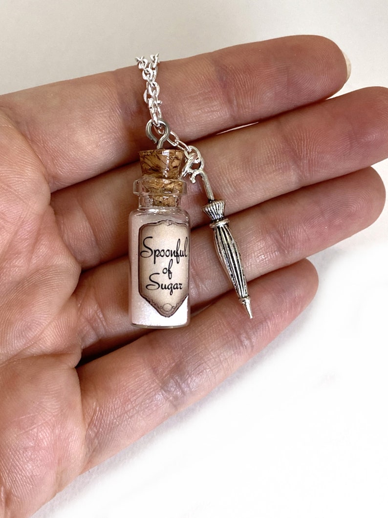 May include: A silver chain necklace with a small glass bottle charm that says "Spoonful of Sugar" and a silver umbrella charm.