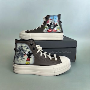 May include: Brown high-top sneakers with white soles and laces. The sneakers feature hand-painted artwork of Mickey and Minnie Mouse in Paris. One shoe has the text "Paris with love". The sneakers are on a gray box.