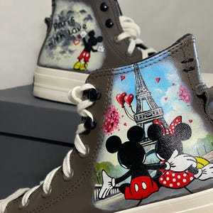 May include: Brown high-top sneakers featuring hand-painted artwork of Mickey and Minnie Mouse in Paris. The design includes the Eiffel Tower, hearts, and the phrase "Paris with love."