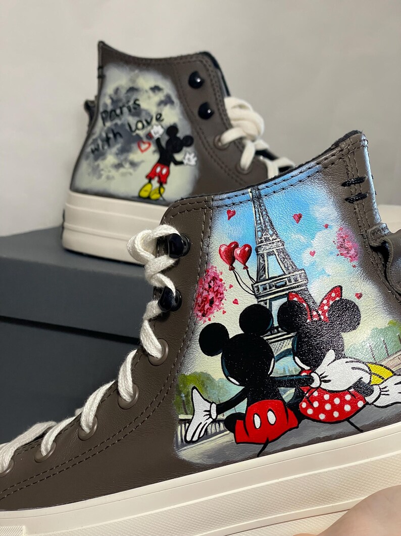 May include: Brown high-top sneakers featuring hand-painted artwork of Mickey and Minnie Mouse in Paris. The design includes the Eiffel Tower, hearts, and the phrase "Paris with love."