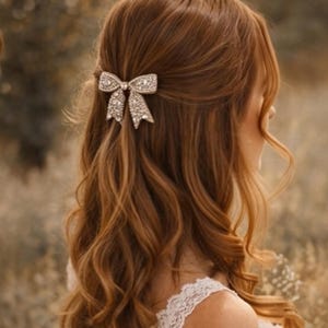 Puede incluir: Una horquilla plateada con forma de lazo, adornada con piedras brillantes, adorna el cabello casta&ntilde;o rojizo ondulado. El fondo es borroso, lo que sugiere un entorno natural. El accesorio para el cabello a&ntilde;ade un toque de elegancia y brillo al peinado.