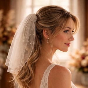 May include: A sheer white bridal veil featuring scattered small pearl embellishments and a finished edge. The veil is attached to a hair accessory and worn with a white lace garment and a single drop earring with a small white stone.