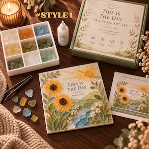 May include: A sea glass art kit titled This Is The Day, featuring a box, a nine-compartment tray of colored sea glass, a bottle of craft adhesive, metal tweezers, a step-by-step guide, and a finished square art piece with sunflowers.