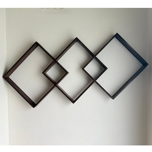 May include: A wall-mounted display unit consisting of three interconnected dark brown wooden square frames arranged in a diamond orientation. The frames are linked at their corners, creating a geometric pattern with open centers.