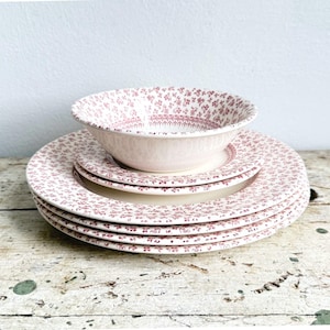 May include: A stack of three round ceramic plates and one bowl featuring a repeating small-scale floral pattern in a muted reddish-pink color on a cream-colored background. The dinnerware set displays a consistent botanical print throughout.