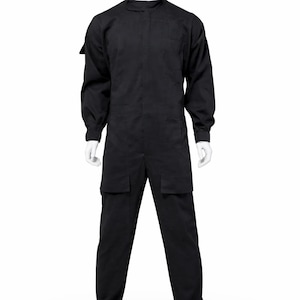 Puede incluir: Mono negro con mangas largas, cuello mandarín y dos bolsillos delanteros. La prenda se exhibe en un maniquí blanco sobre un fondo blanco. El mono parece estar hecho de una tela duradera.