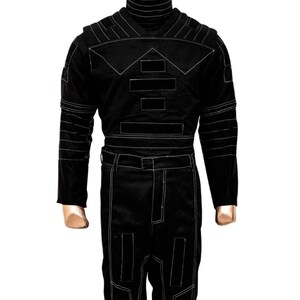 K&ouml;nnte beinhalten: Schwarzer Overall mit wei&szlig;en Steppn&auml;hten. Das Outfit hat einen hohen Rollkragen, lange &Auml;rmel und eine taillierte Silhouette. Wei&szlig;e N&auml;hte umrei&szlig;en geometrische Formen auf Brust, Schultern und Beinen. Der Overall hat einen G&uuml;rtel und einen Rei&szlig;verschluss.