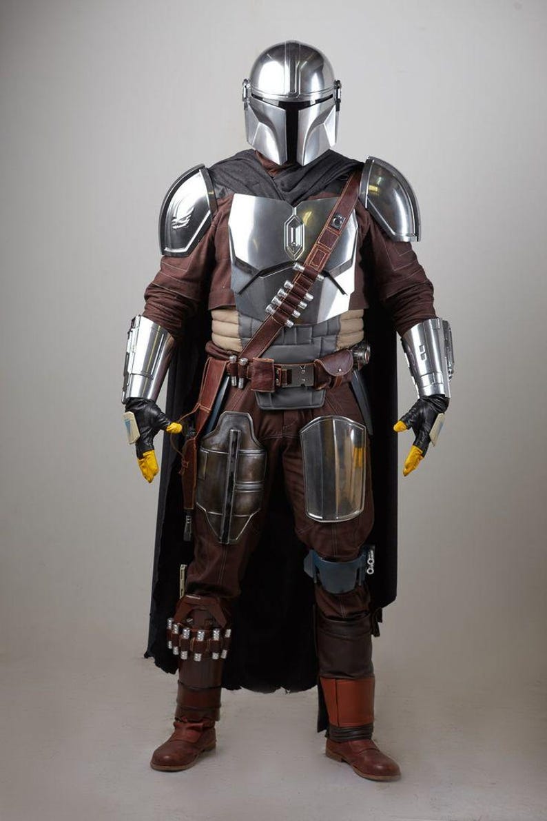 May include: Full-body shot of a detailed costume inspired by a science fiction character. The costume features a silver helmet, chest armor, and arm guards. The outfit includes brown pants, boots, and a black cape, with yellow gloves and a utility belt.
