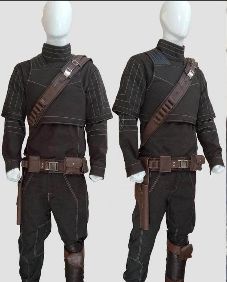 May include: Two black costumes with brown detailing are displayed on mannequins. Each outfit features a high-collared top, trousers, and a utility belt with pouches. A brown shoulder strap with ammunition holders and a holster are also included. White stitching details the seams.