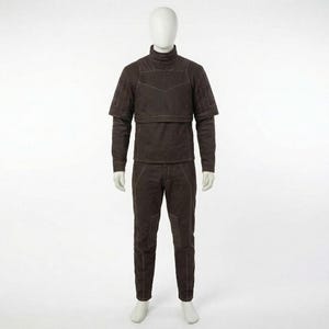May include: A brown quilted jumpsuit on a mannequin. The outfit features a high-neck top with shoulder detailing and long sleeves, and matching trousers. White stitching highlights the seams and panels of the garment.