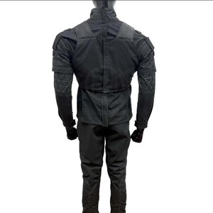 May include: A black tactical jacket and pants set. The jacket features reinforced shoulder and elbow patches, with a high collar and multiple pockets. The pants have a slim fit. The outfit is designed for durability and functionality.