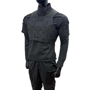 May include: Black tactical outfit displayed on a mannequin. The outfit includes a high-neck shirt, a vest with rectangular panels, long sleeves, and matching pants. The ensemble is designed for a sleek, functional aesthetic.