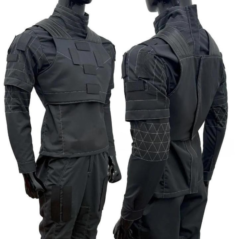 May include: Black tactical outfit displayed on a mannequin. The outfit includes a high-collared shirt, a vest with rectangular panels, and matching pants. The sleeves and upper back feature geometric stitching. The mannequin is wearing black gloves.