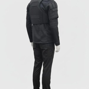 Puede incluir: Un conjunto t&aacute;ctico negro, que incluye una chaqueta con hombreras y un chaleco, y pantalones cargo a juego. El conjunto se exhibe en un maniqu&iacute;. La chaqueta tiene m&uacute;ltiples bolsillos y un cuello alto. Los pantalones tienen bolsillos laterales.