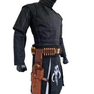 Op de afbeelding: Zwart kostuum met witte stiksels, met een hoge kraag en een gereedschapsriem met bruine accenten. Een bruin holster is aan de riem bevestigd. Het kostuum bevat een zwarte rok met een wit embleem. Dit is een cosplay-outfit.