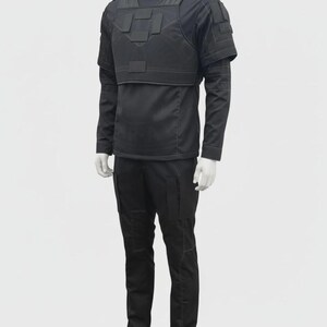 Puede incluir: Traje t&aacute;ctico negro sobre un maniqu&iacute;. El traje incluye una camisa de manga larga, un chaleco t&aacute;ctico y pantalones. El chaleco tiene m&uacute;ltiples paneles rectangulares. Los pantalones tienen bolsillos en los muslos. El traje se muestra sobre un fondo blanco.