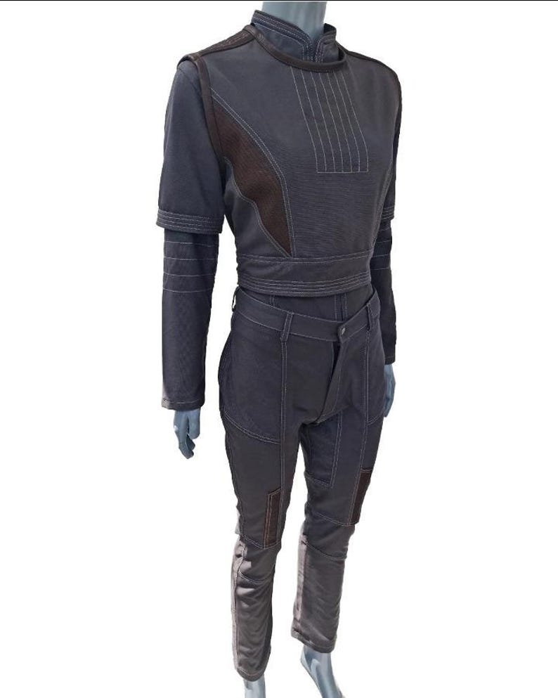 May include: A two-piece dark grey outfit on a mannequin. The top is a cropped jacket with a high collar and long sleeves. The pants are high-waisted with pockets and patches. White stitching details the seams and accents the design.