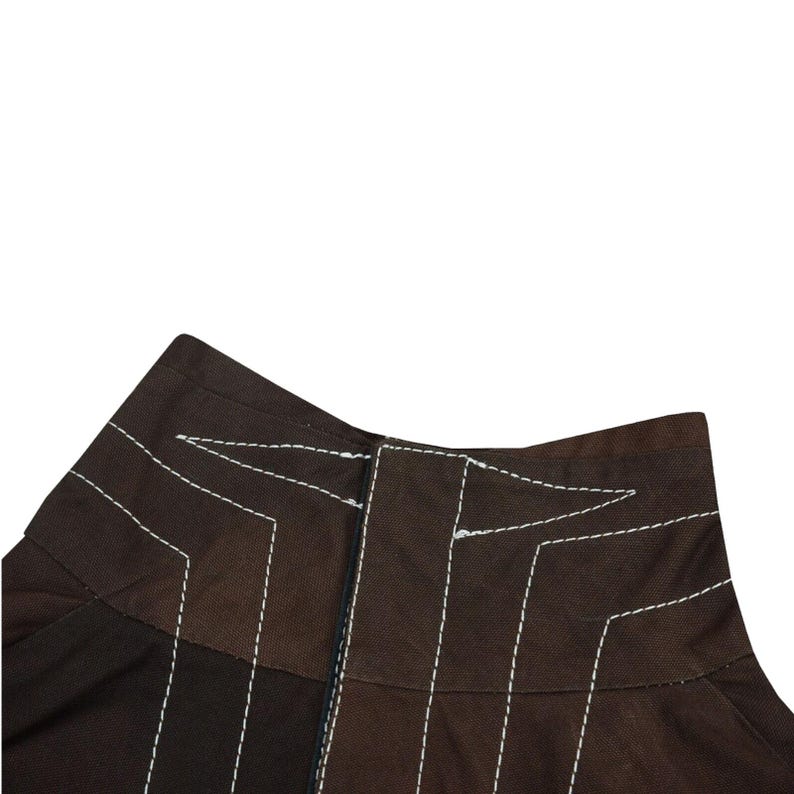 May include: Close-up of a brown garment with white stitching. The stitching creates geometric patterns and outlines the seams. The fabric appears to be a medium-weight material.