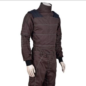 May include: Brown racing suit with white stitching and a high collar. The suit features black accents on the shoulders and cuffs. The long-sleeved jumpsuit has a fitted waist and is designed for motorsports.
