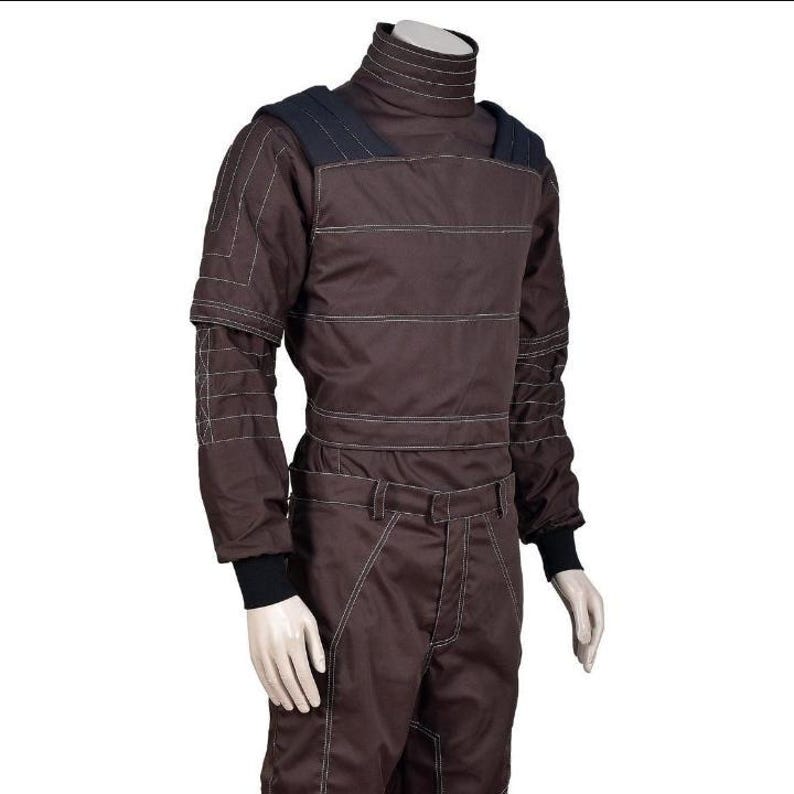 May include: Brown racing suit with white stitching and a high collar. The suit features black accents on the shoulders and cuffs. The long-sleeved jumpsuit has a fitted waist and is designed for motorsports.