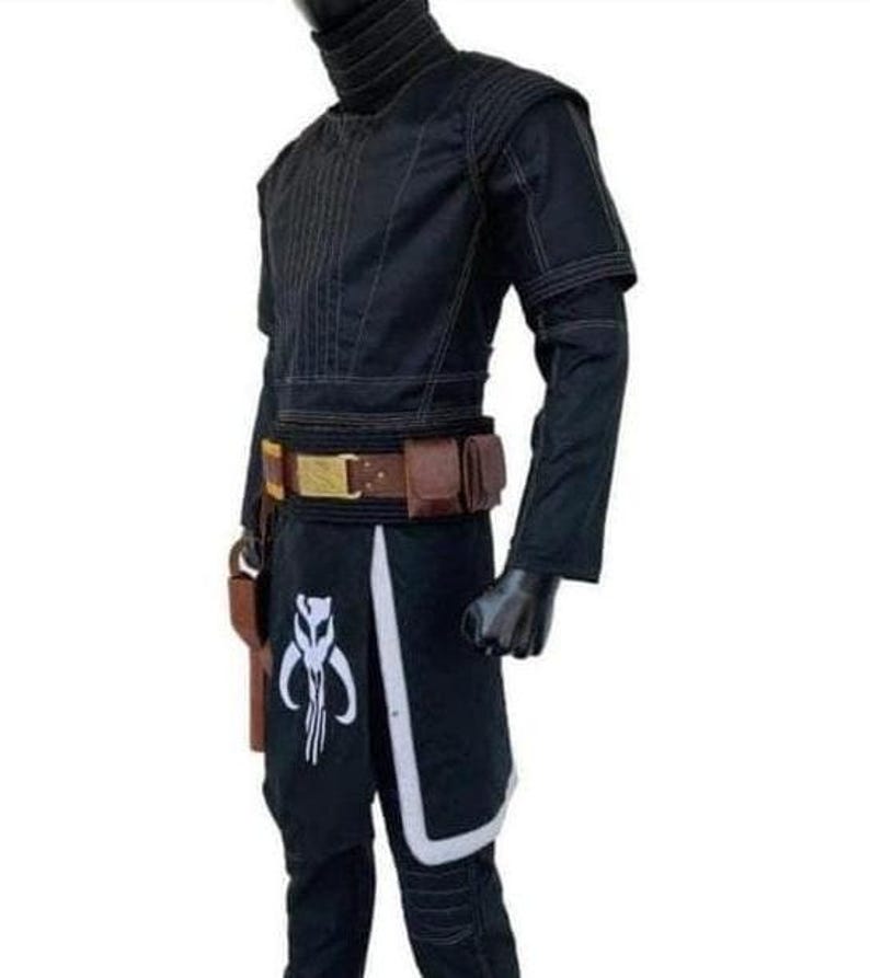 Op de afbeelding: Zwart kostuum met een hoge kraag, bruine riem met zakjes en een holster. De broek heeft een wit en zwart ontwerp met een symbool. Het kostuum wordt op een mannequin gepresenteerd.