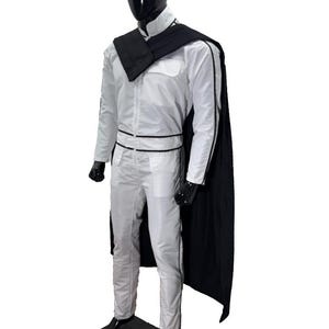 K&ouml;nnte beinhalten: Ein wei&szlig;er Overall mit schwarzen Zierleisten und einem schwarzen Umhang wird auf einer Schaufensterpuppe pr&auml;sentiert. Das Outfit umfasst einen hohen Kragen, einen schwarzen G&uuml;rtel und schwarze Handschuhe. Die Schaufensterpuppe hat einen schwarzen Kopf und steht auf einer schwarzen Basis.