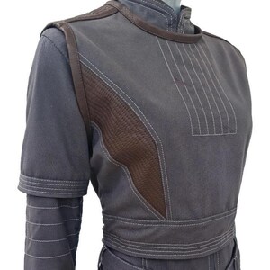 May include: A gray jacket with brown leather accents and white stitching. The jacket features a high collar, short sleeves, and a fitted waist. The brown leather is on the shoulders and the side of the jacket.